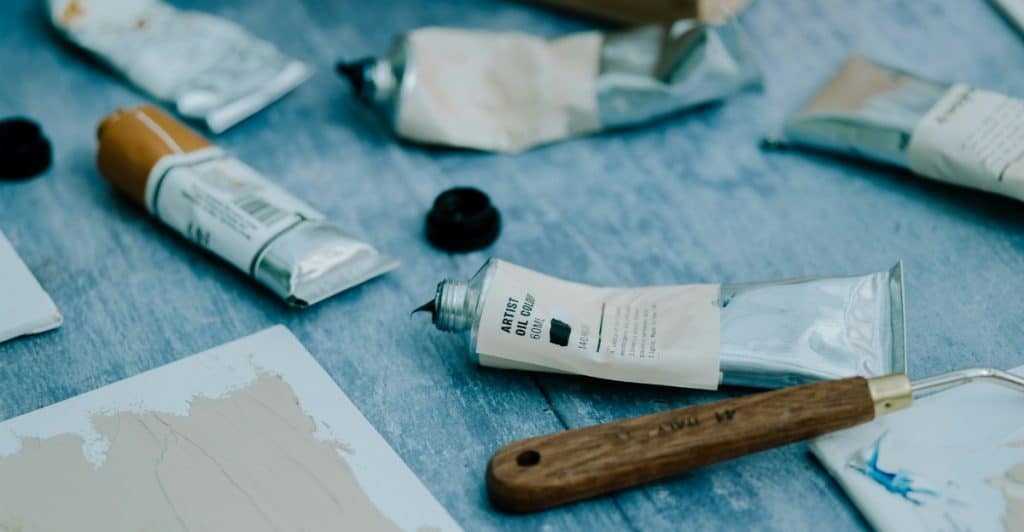 Painting supplies, including tubes of paint and a palette knife, arranged on a table.