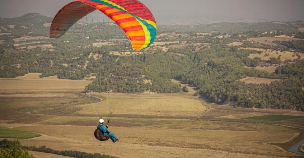 A paraglider flying over a rural landscape.