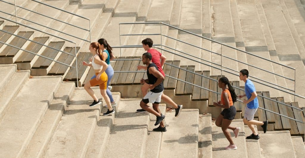 Group of young adults running up outdoor stadium steps during a fitness workout.