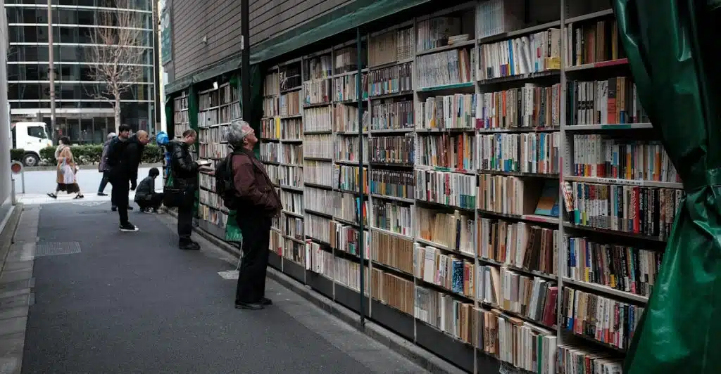 Several people browsing books at an outdoor bookstore with shelves lining an alleyway.