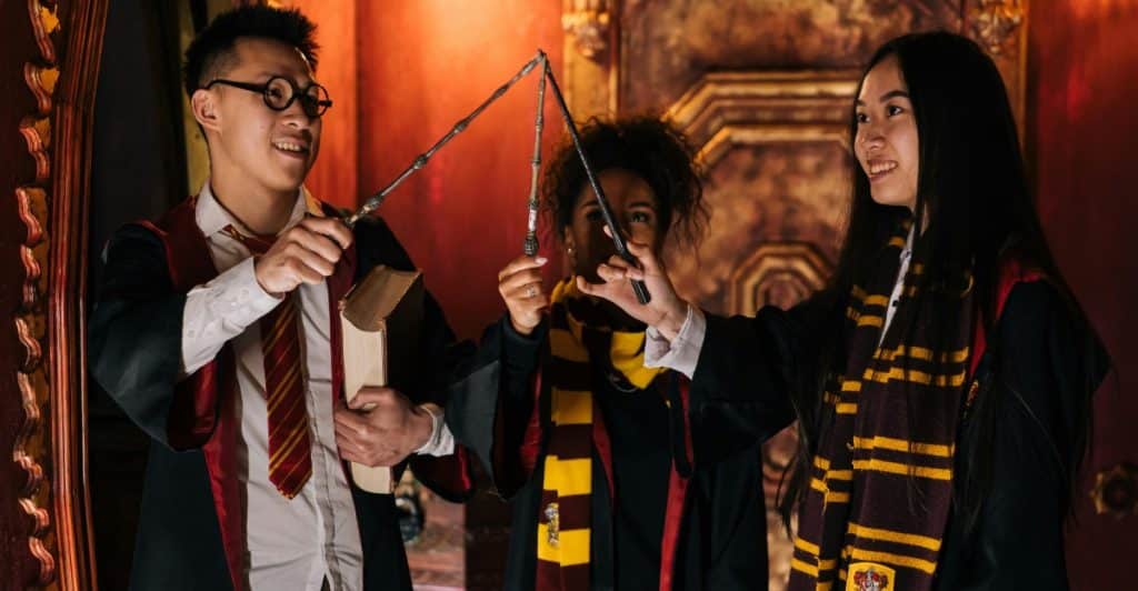 Three people dressed in Harry Potter-themed attire holding wands in a decorated room.