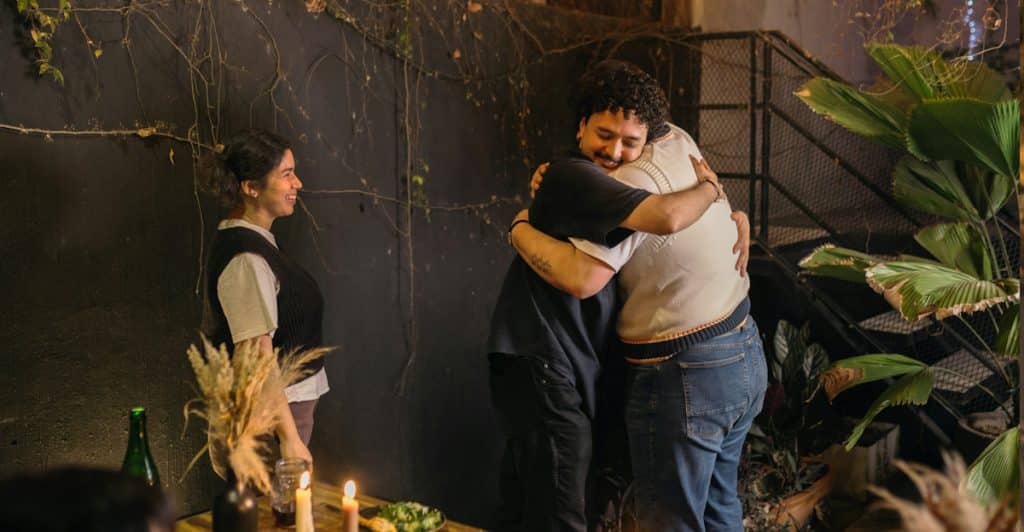 Two people hugging outdoors, with another person standing nearby.