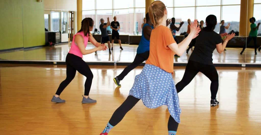 A group of people participating in a low-impact exercise class in a gym with wooden floors.