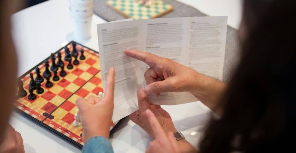 Two people looking at a game instruction sheet with a chessboard nearby.