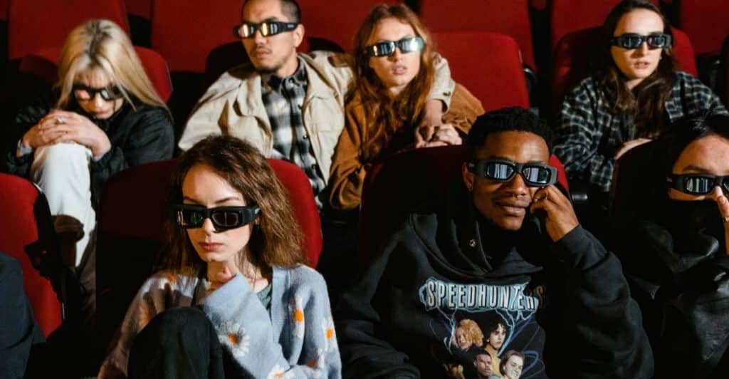 A group of people wearing 3D glasses sit in a movie theater.