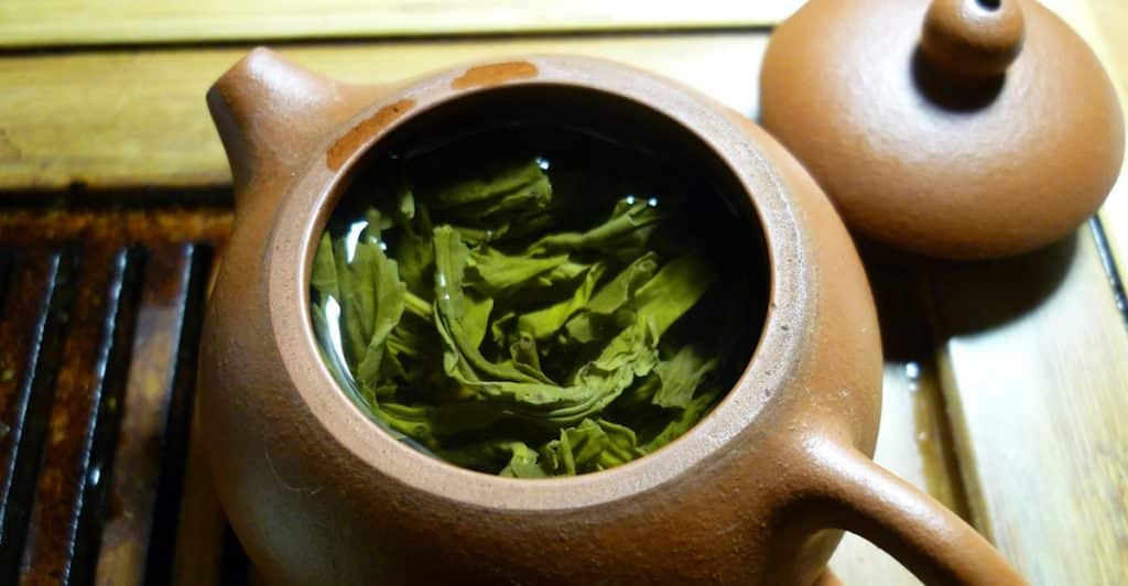 Green tea leaves steeping in a brown teapot.