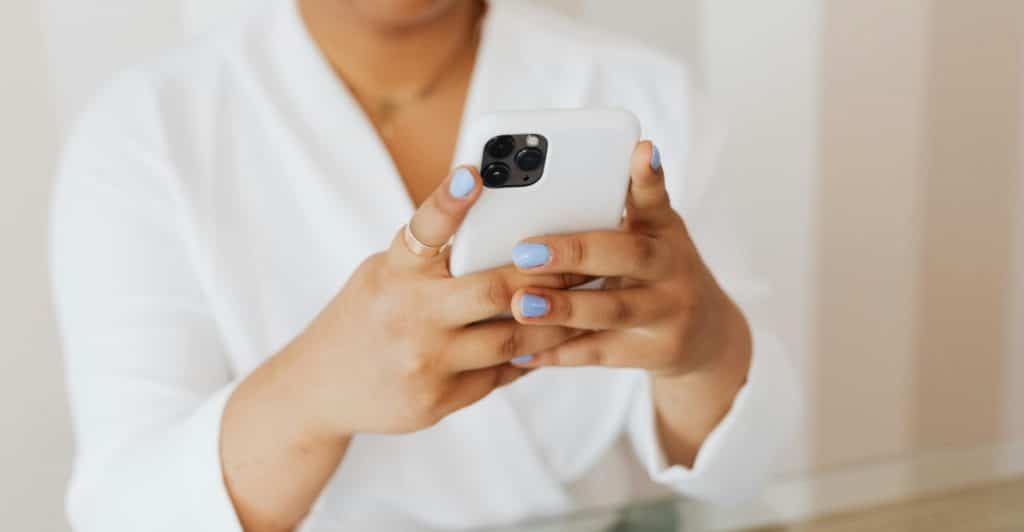 A person with light blue nail polish is holding a white smartphone, with a neutral background.