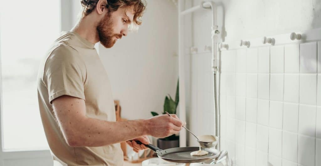 A man carefully pouring batter onto a frying pan over a gas stove