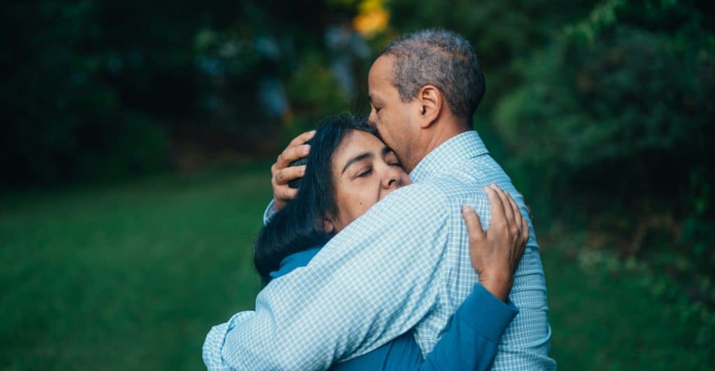 One person embracing another person outdoors in a lush green garden.