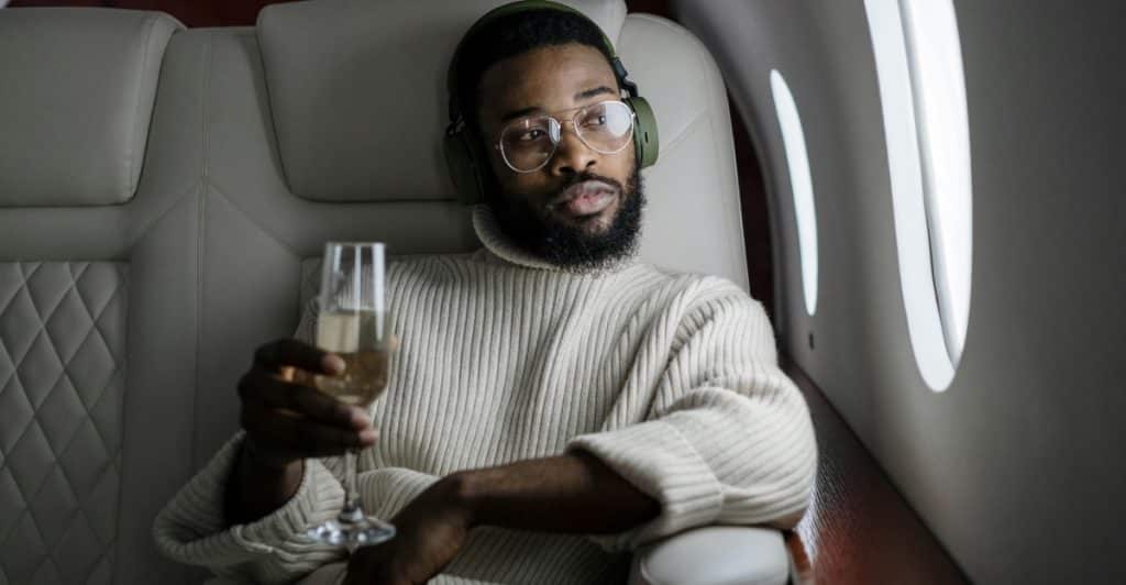 A person sits in a luxurious airplane seat, holding a drink and looking out the window.