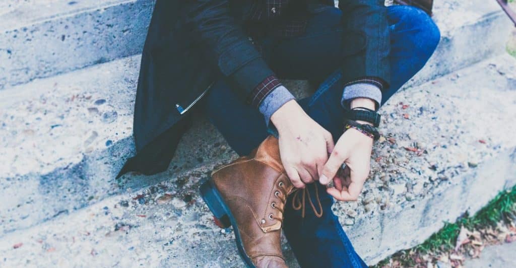 A person sitting on concrete stairs, wearing jeans, a dark jacket, and brown boots.