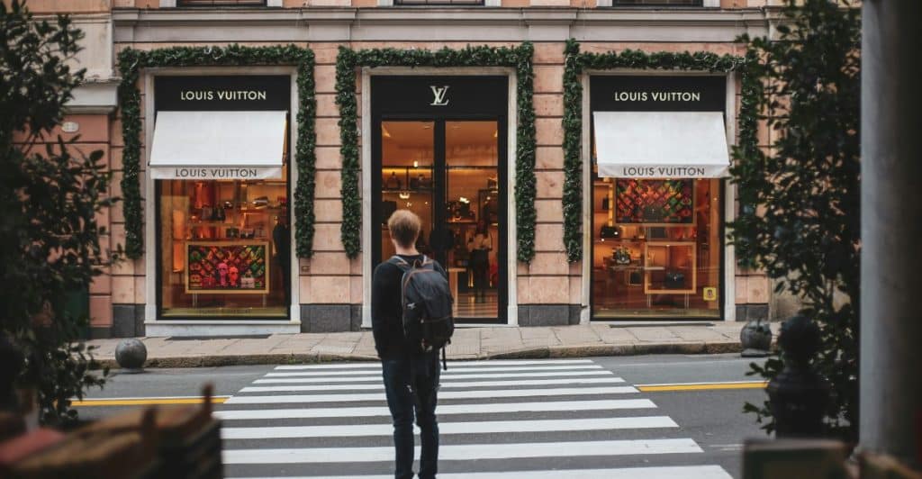 A person standing on a crosswalk looking at a Louis Vuitton store.