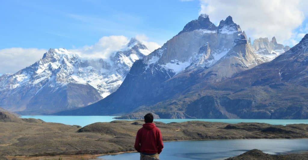 A person wearing a red jacket standing on a rocky outcrop, looking out at a lake and mountains.