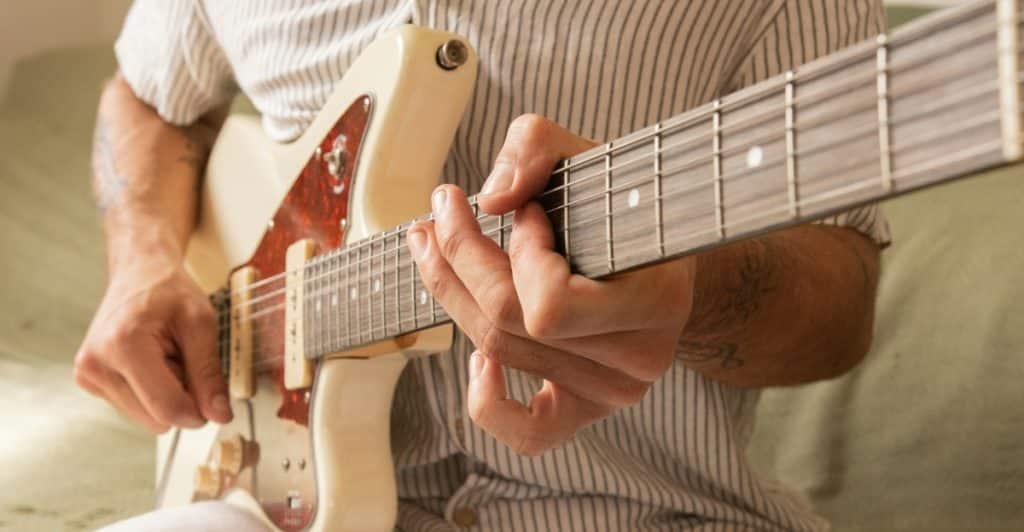 Close-up of a person's hands playing chords on an electric guitar.