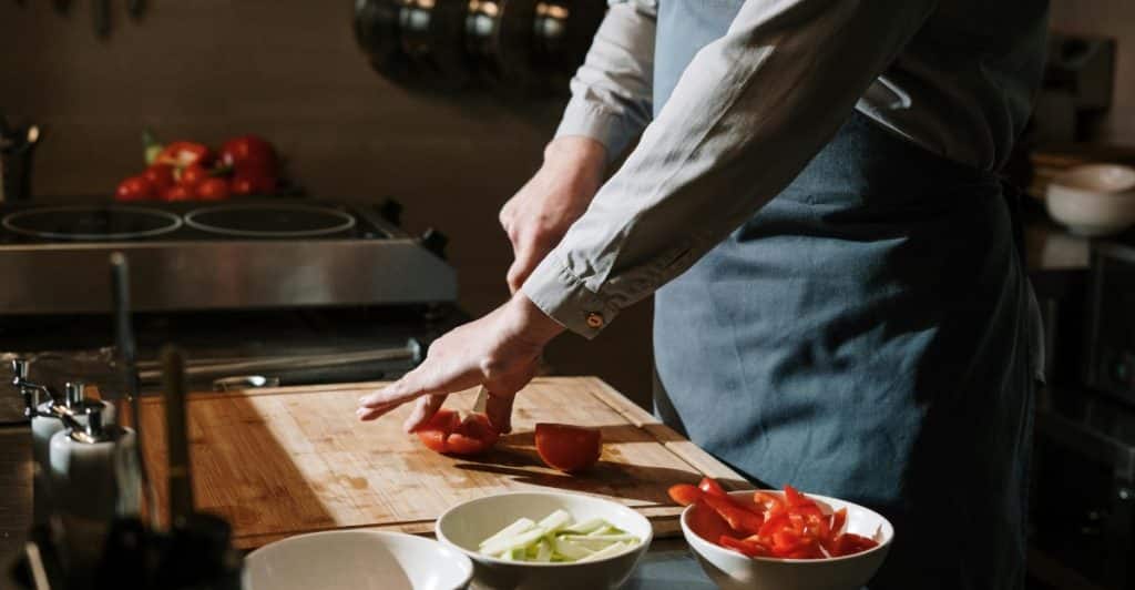 A person wearing an apron chopping vegetables on a cutting board in a kitchen.