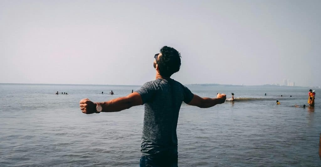 A person standing in the ocean with arms outstretched, facing away from the viewer.