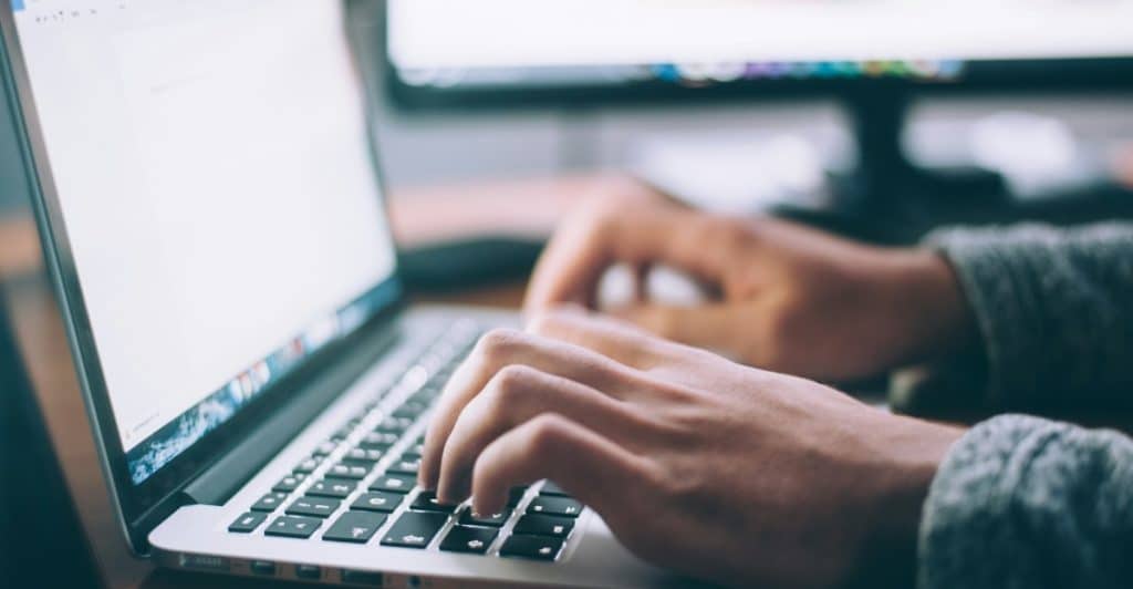 A person's hands typing on a laptop keyboard.