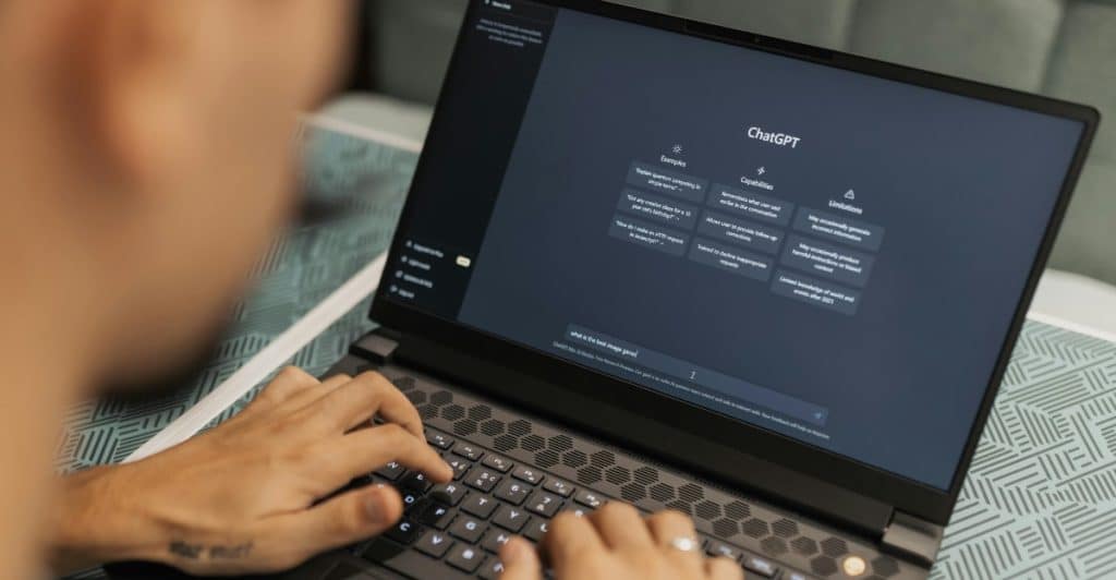 A person is typing on a laptop with the ChatGPT interface visible on the screen.