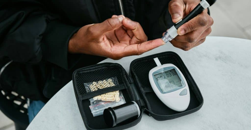 A person with dark skin using a blood glucose meter on their fingertip.