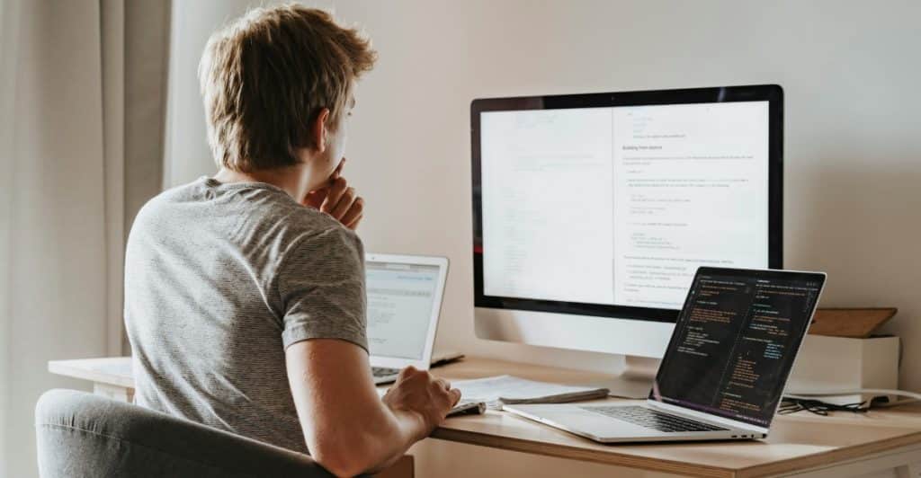 A person working at a desk with a monitor and two laptops.