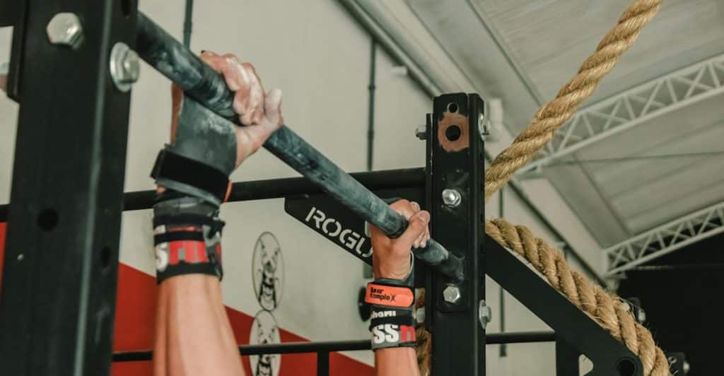 A person's hands gripping a pull-up bar in a gym setting.