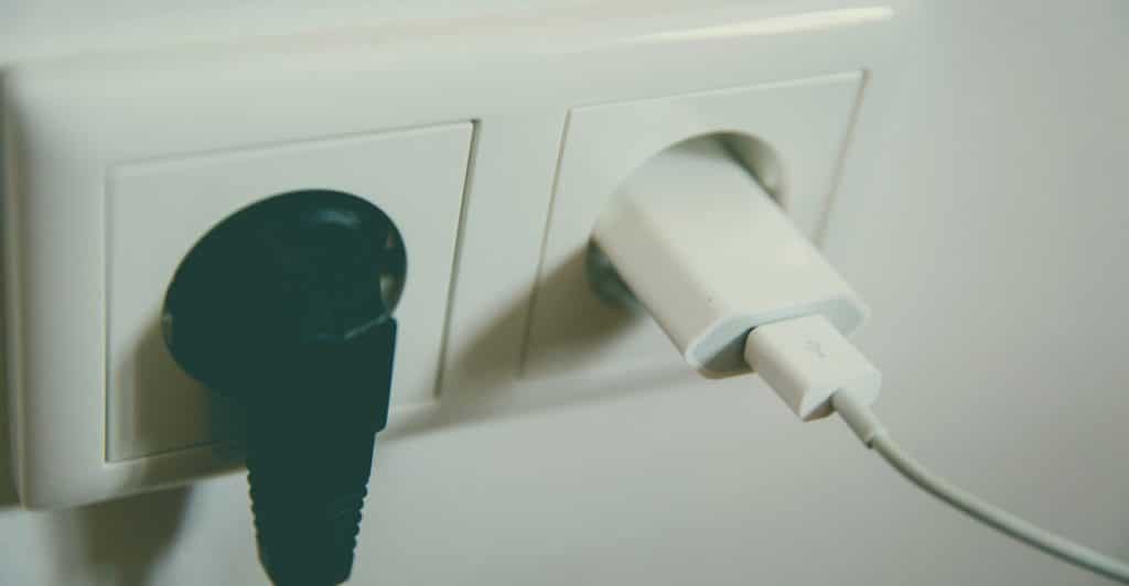 A close-up of two electrical outlets, one with a black plug inserted and the other with a white USB charger plugged in.