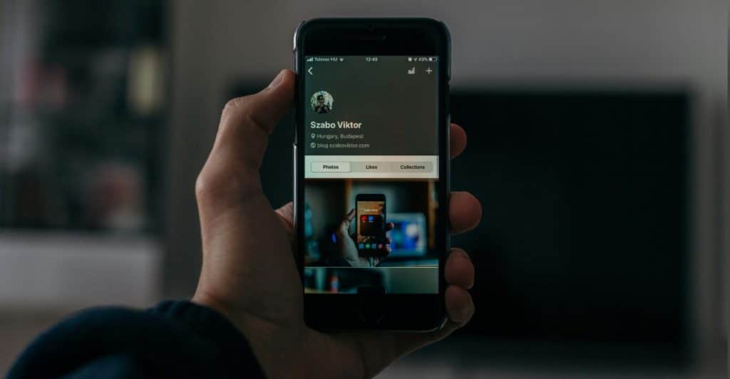 Close-up of a hand holding a smartphone displaying a social media profile page with photos.