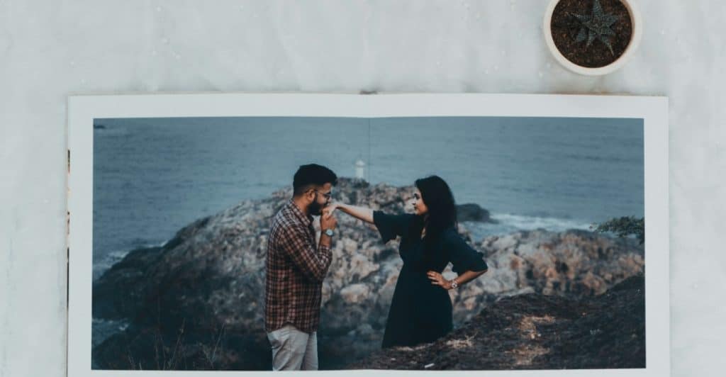 A photograph of a couple standing on a rocky cliff overlooking the ocean, placed in an open photo album next to a potted plant, representing shared memories and reliability.