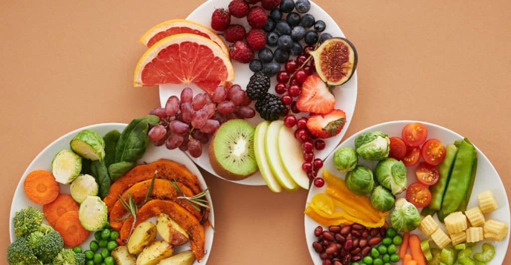 Overhead shot of three white plates filled with a variety of colorful fruits and vegetables.