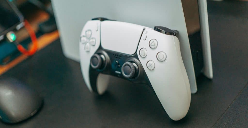 Close-up of a white PlayStation 5 video game controller next to the console.