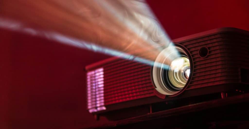 A projector emitting a beam of light in a dark room with a red wall.