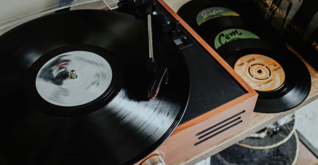A close-up of a record player with a black vinyl record on the turntable and several other records stacked beside it.