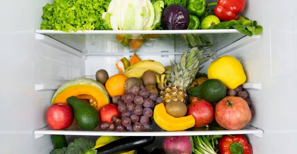An open refrigerator filled with various fresh fruits and vegetables on the shelves.