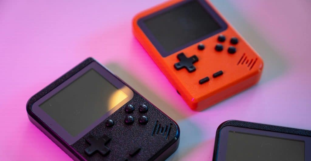 Three retro handheld game consoles are displayed on a pink surface.