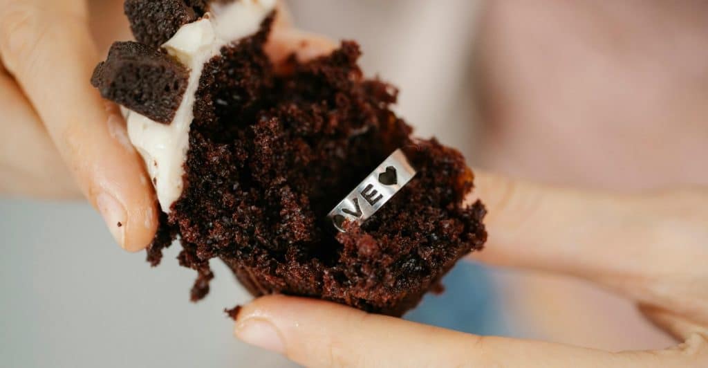 A person holding a cupcake with a ring hidden inside.