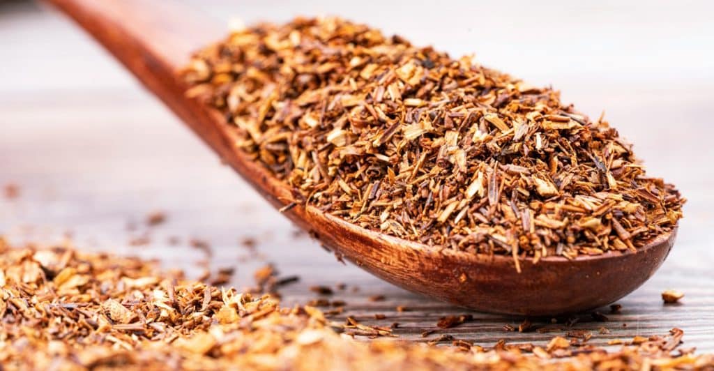 Rooibos tea leaves on a wooden spoon.