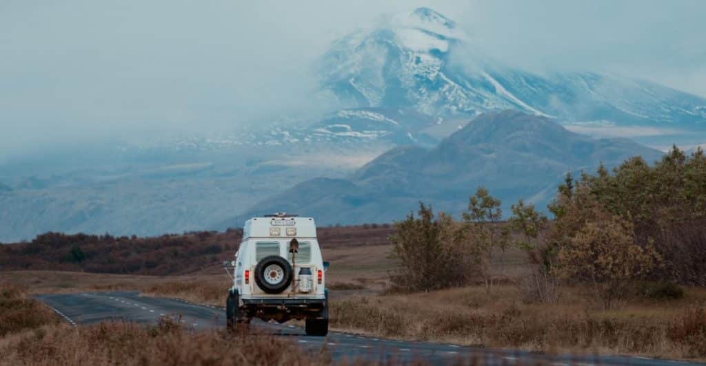 4x4 camper SUV driving through rugged Icelandic terrain with distant volcanoes and glaciers.