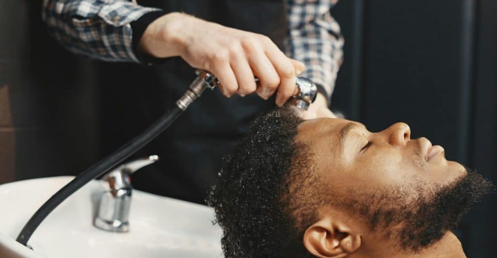A barber is rinsing a client's hair in a salon sink.