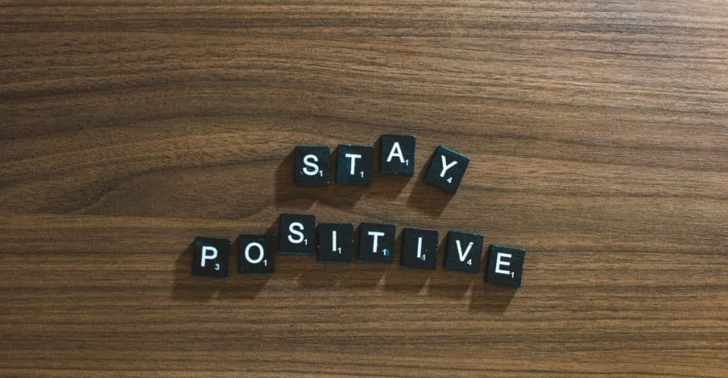 Scrabble tiles are arranged on a wooden surface to spell out the phrase "Stay Positive".