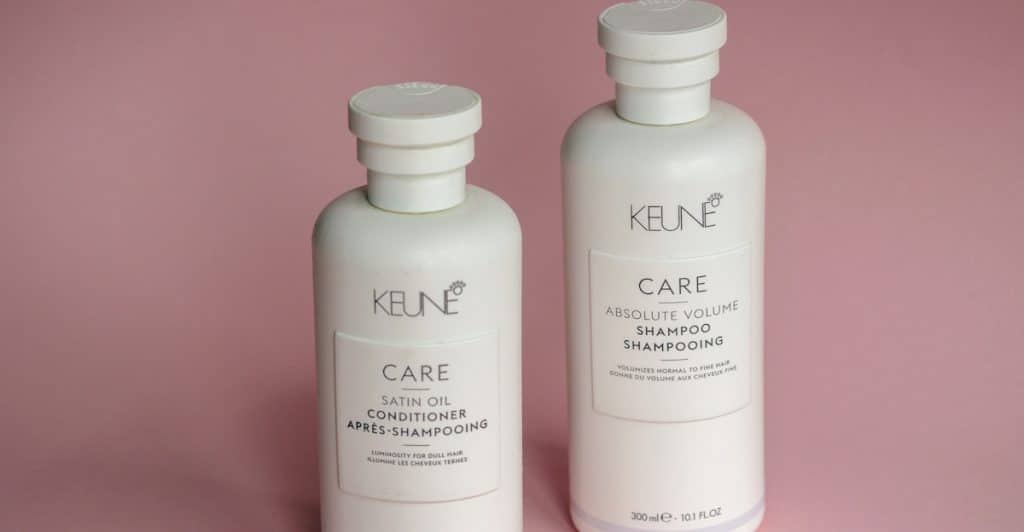 Two bottles of hair care products, one shampoo and one conditioner, on a pink background.