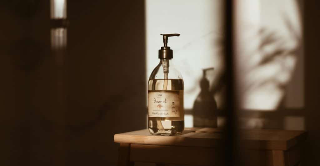 A bottle of shower oil sitting on a small wooden stool in a dimly lit setting.