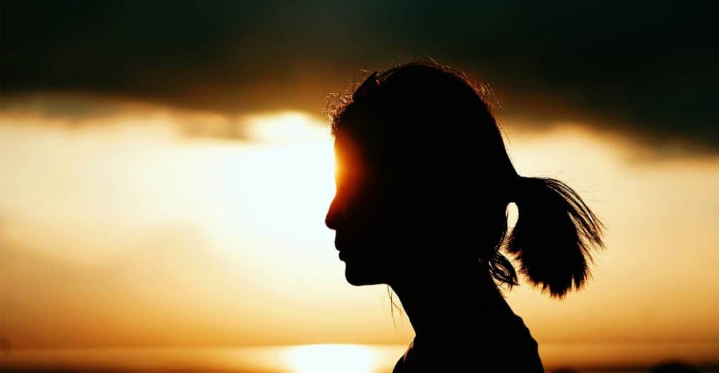 The silhouette of a woman's head and shoulders against a bright sunset.