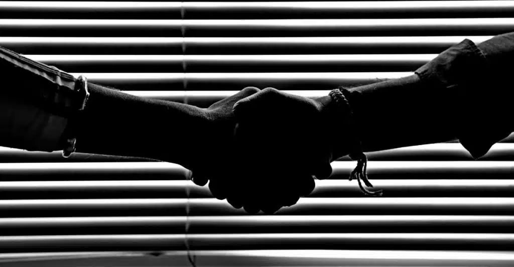 A black and white, close-up silhouette of two people shaking hands against a striped background.
