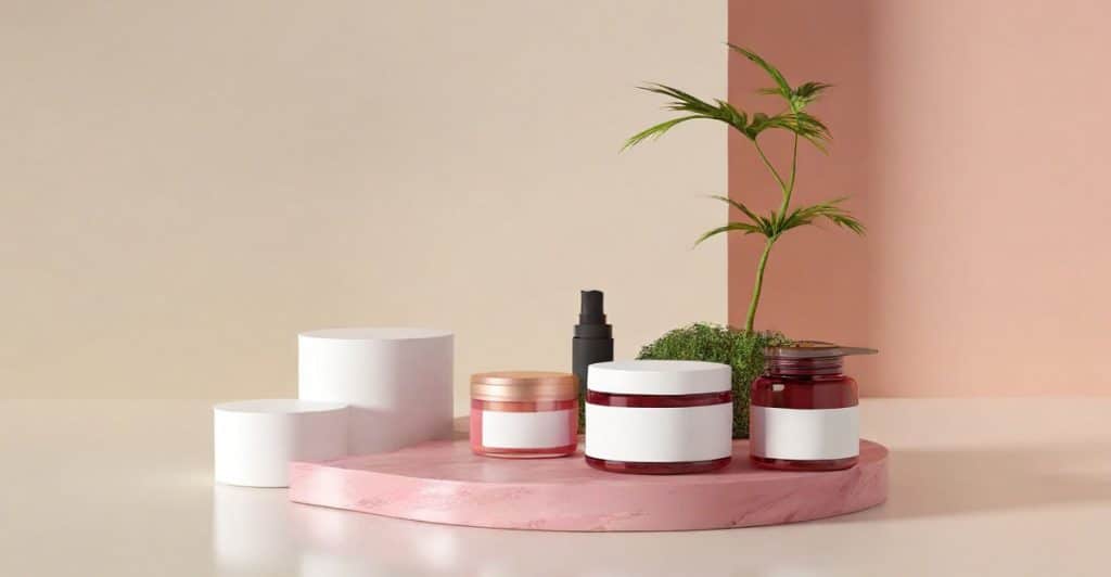 Skincare product containers are displayed on a pink stand with plants and white cylindrical risers.