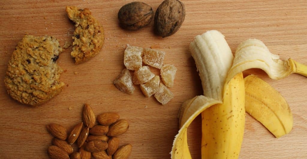 A peeled banana, almonds, walnuts, and other foods arranged on a wooden cutting board.