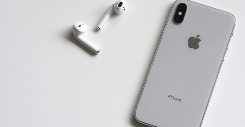 A silver smartphone and white wireless earbuds are placed on a clean, white background.