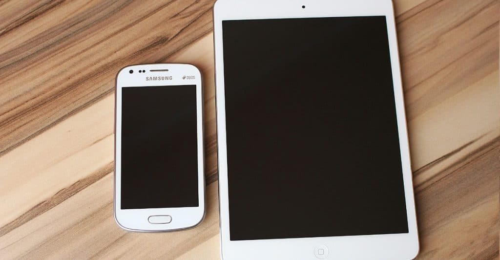 A white smartphone and a white tablet are displayed side-by-side on a wooden table.