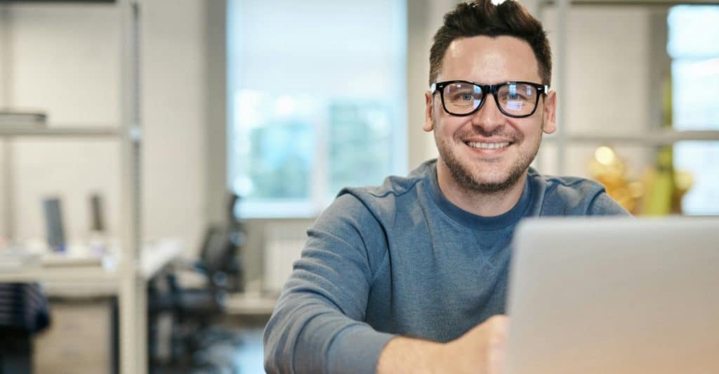 Smiling man wearing glasses working on a laptop in a modern office setting