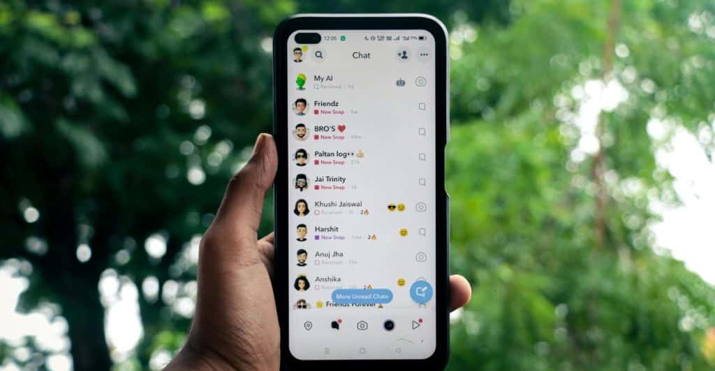 A hand holding a smartphone displaying the Snapchat chat interface with a list of contacts.