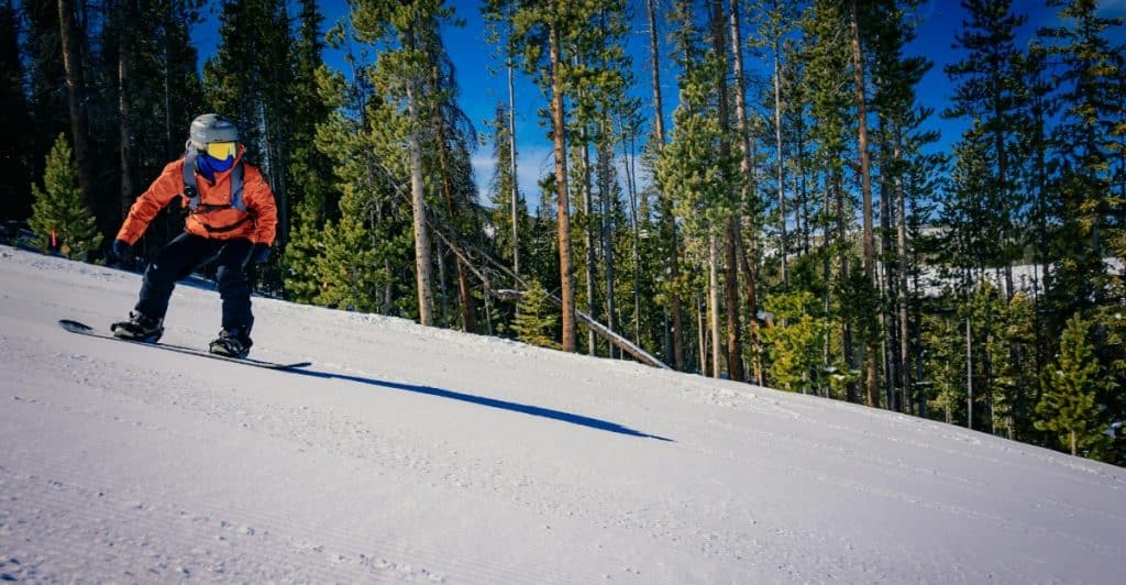 A snowboarder riding down a snow-covered slope surrounded by trees.